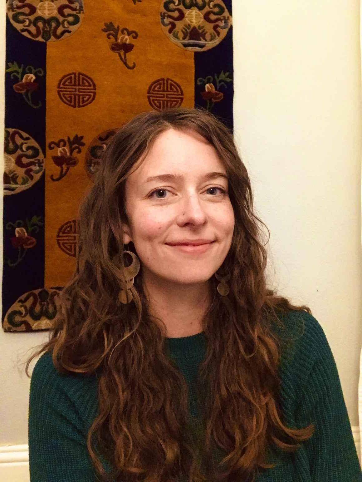 凯特Falkenhart, 科罗拉多州ACLU的运营经理, 微笑, in front of light-colored wall with a brown and black tapestry hanging